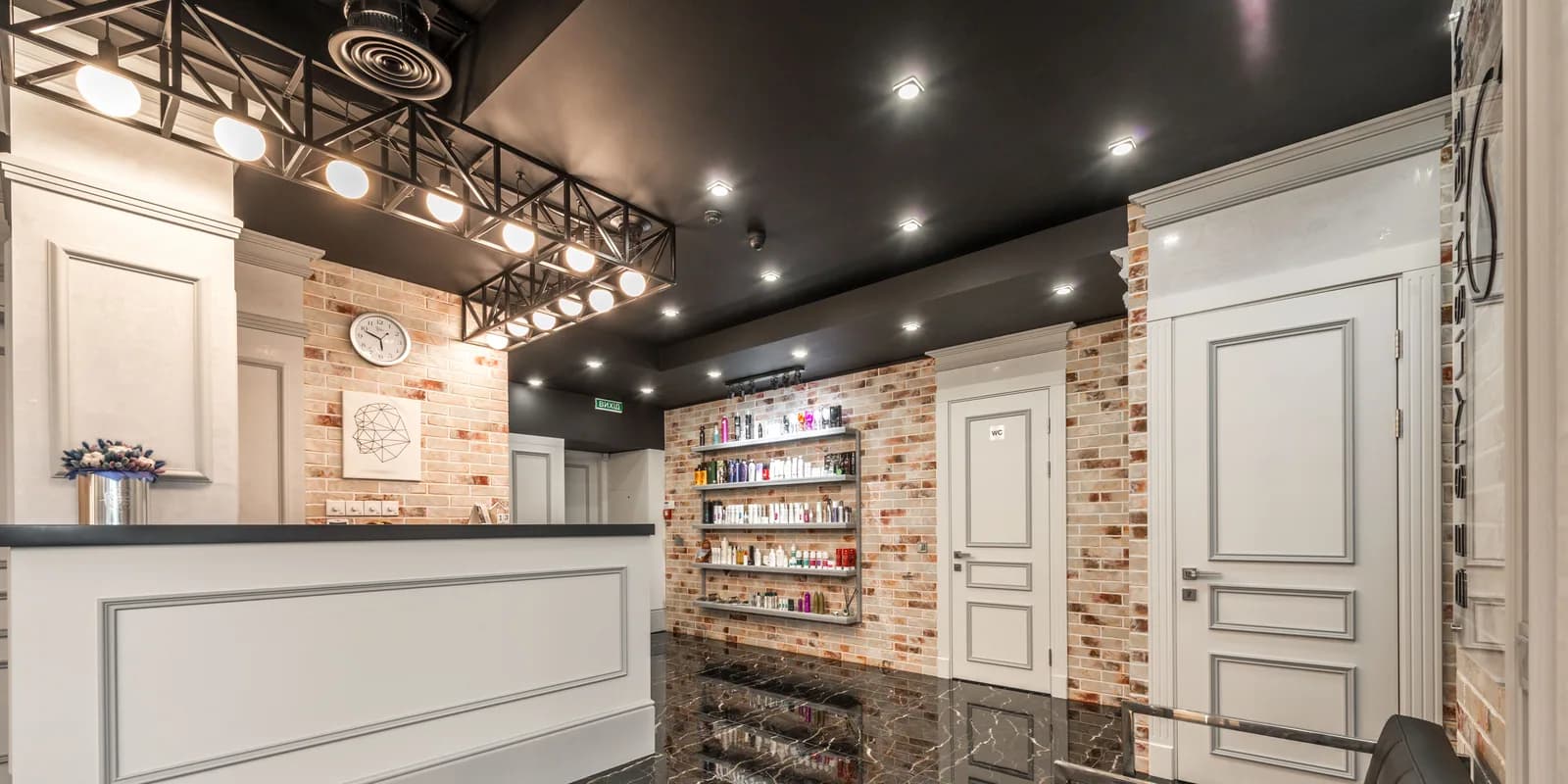 The empty reception desk of a beauty studio, a clock on the brick wall behind it.