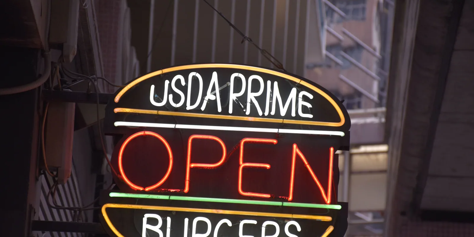 A neon “Open” sign in a burger restaurant’s window, lit at dusk.