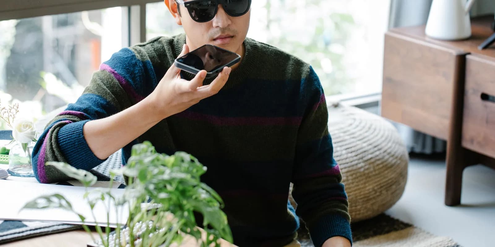A man in sunglasses speaking a question into his phone, held flat in front of him.