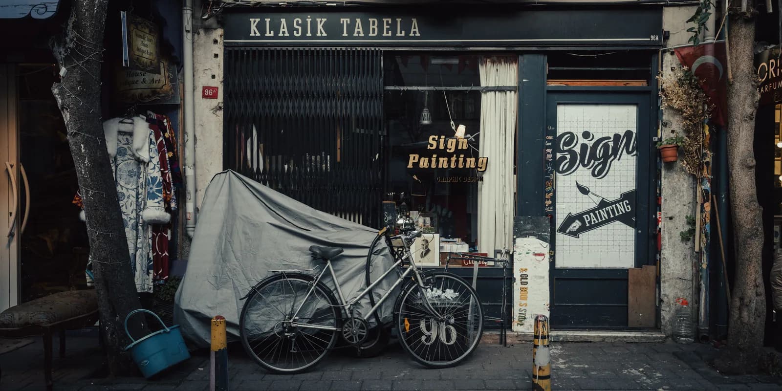 A sign painter’s shop front — the name on a permanent sign over the window, the street number by the door.