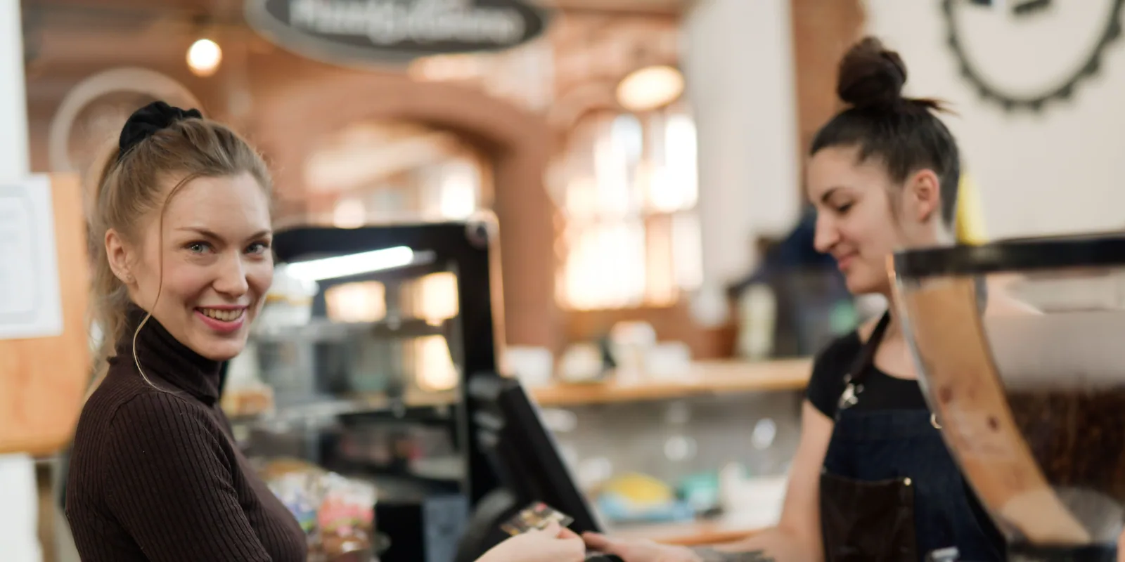 A customer paying at a café counter while the barista rings her up.