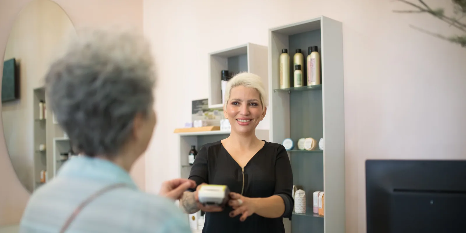 A customer paying at the counter of a barbershop while the barber rings him up.
