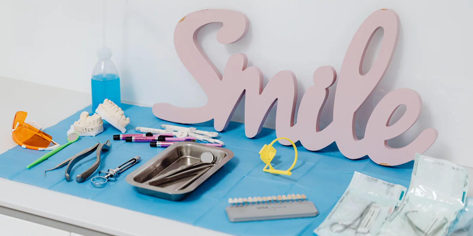 A dental tray — instruments, a shade guide, a model of teeth — under a wooden “Smile” sign.